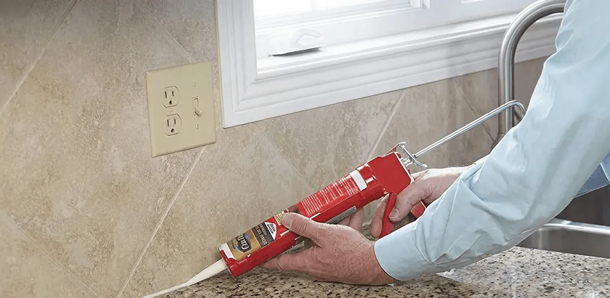 Handyman applying caulk along a kitchen backsplash and countertop seam in Anchorage, AK
