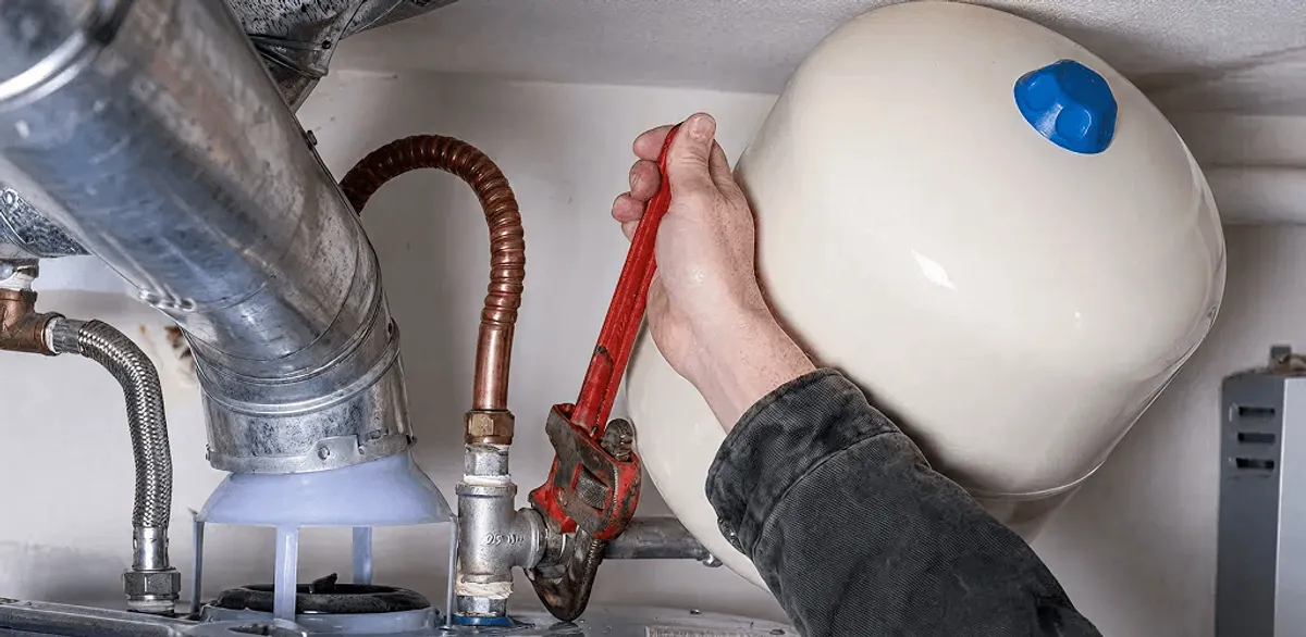 Water heater repair technician tightening plumbing connections near a tank unit in Anchorage, AK